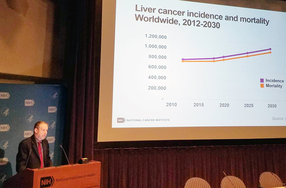 Lowy at podium with slide showing liver cancer incidence projected beside him